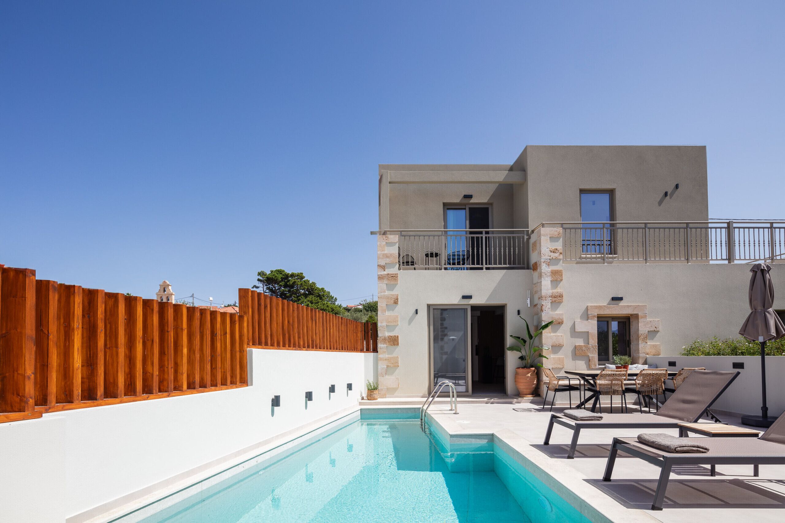 Zona de piscina moderna amb una piscina blava cristal·lina, gandules i una tanca de fusta.
