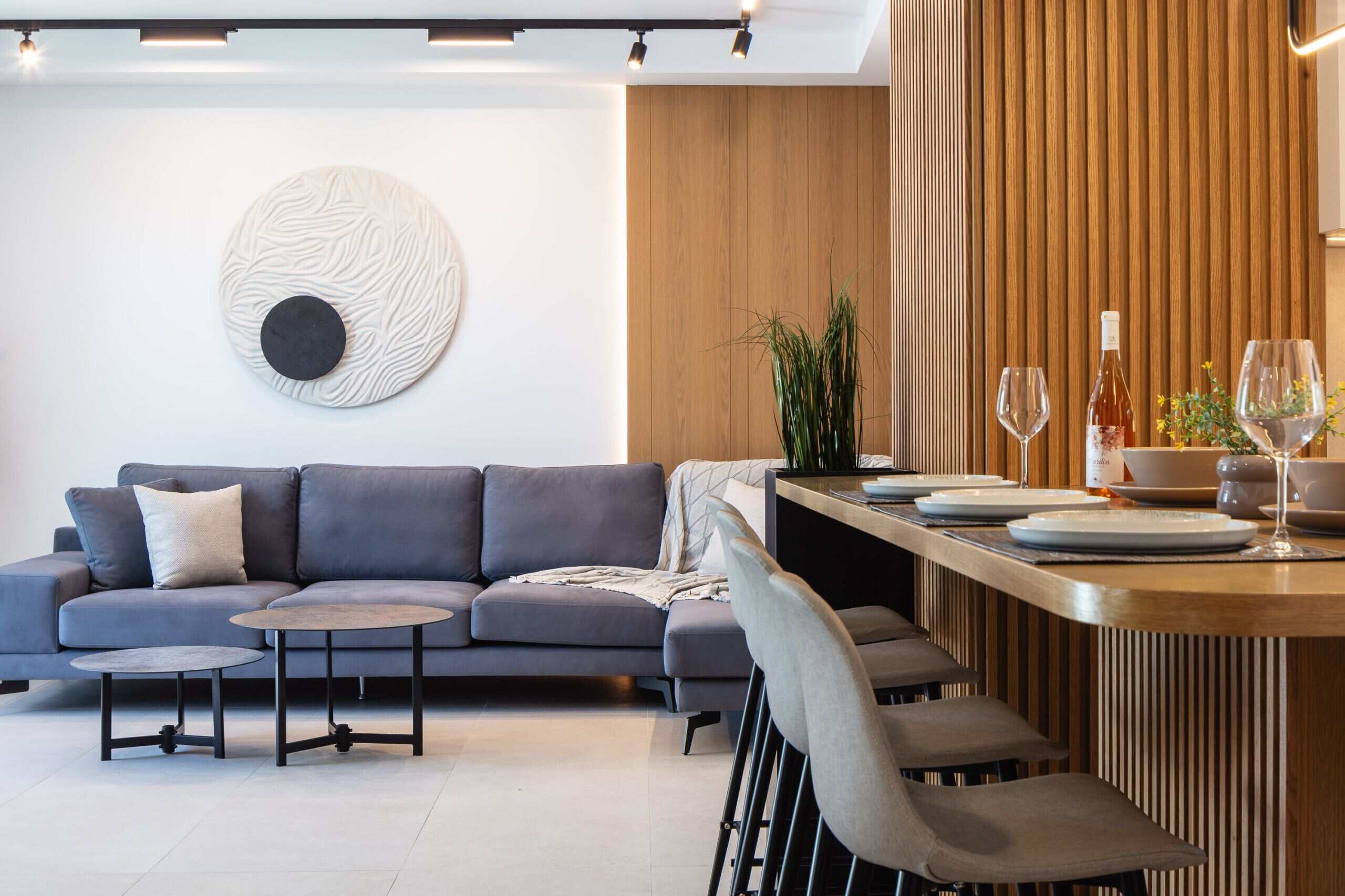 A modern living room with a grey sofa, a round coffee table, and a dining area with a wooden table and chairs.