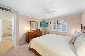 Une chambre à coucher comprenant un lit, une commode, un miroir, un ventilateur de plafond et un téléviseur fixé au mur.