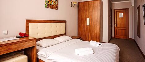 A hotel room with a bed, a desk, a telephone, a wardrobe, and a painting on the wall.