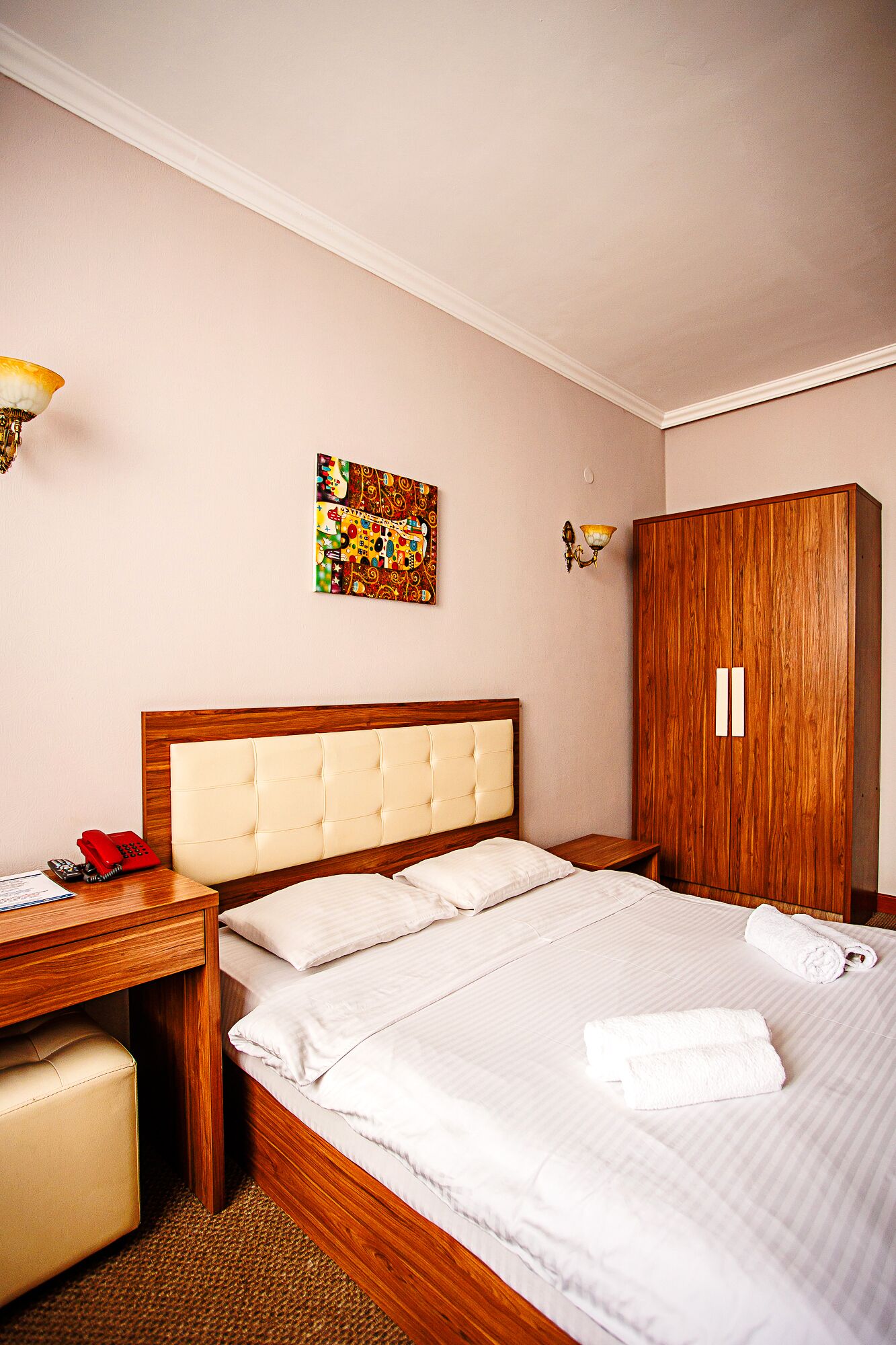 Une chambre d’hôtel comprenant un lit, une armoire en bois, une table de chevet avec un téléphone et une œuvre d’art murale.