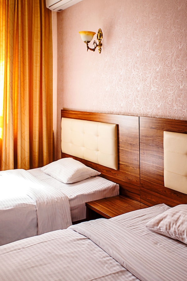 A hotel room with two beds, a wooden headboard, a nightstand, and a wall-mounted lamp. - Korsar hotel (Astana)