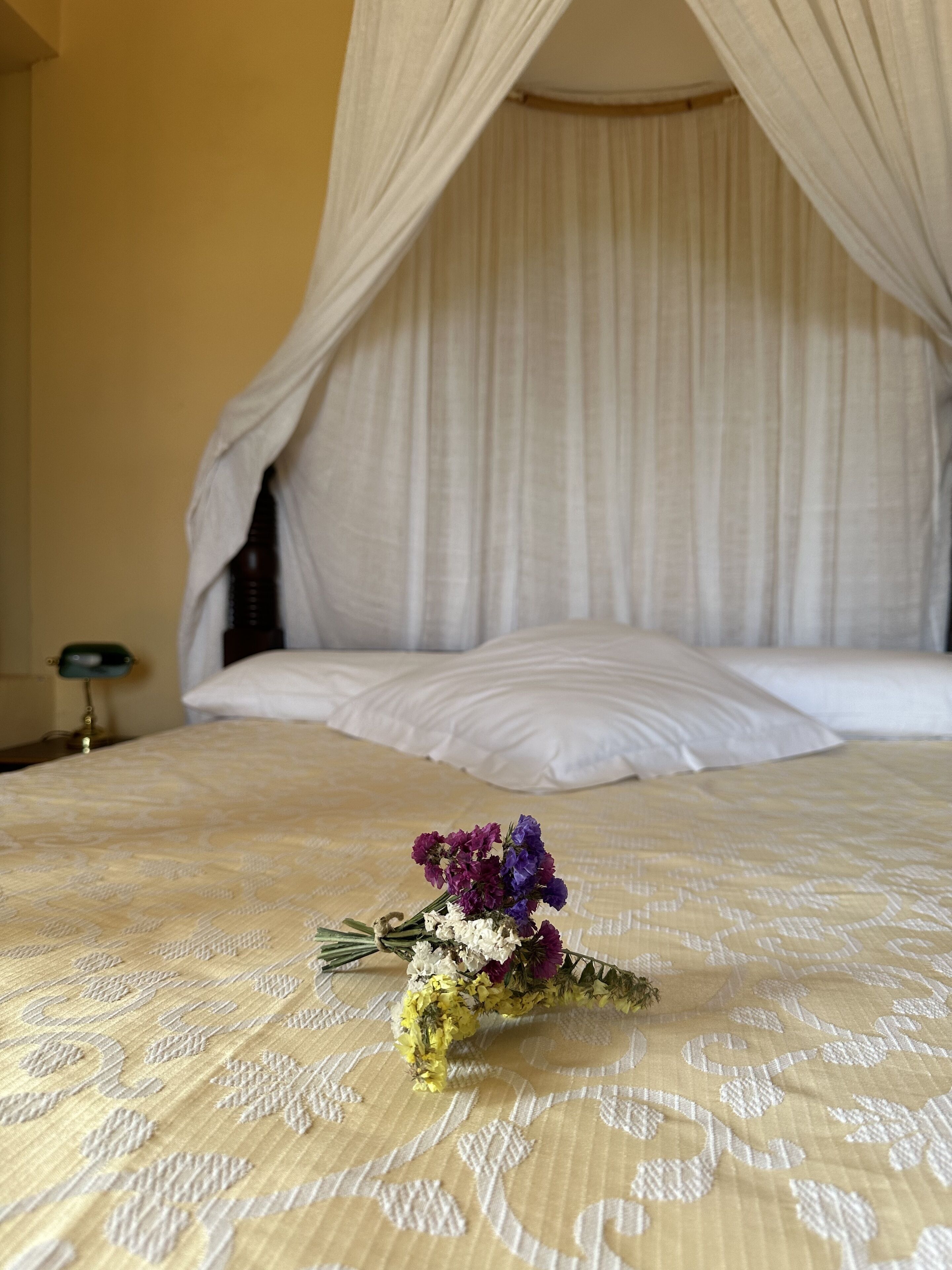 A bed with a canopy, a bedside table with a lamp, and a bouquet of flowers on the bed.