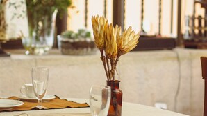 Une table mise pour le repas, avec un vase de fleurs séchées, un verre d’eau et une tasse de café.