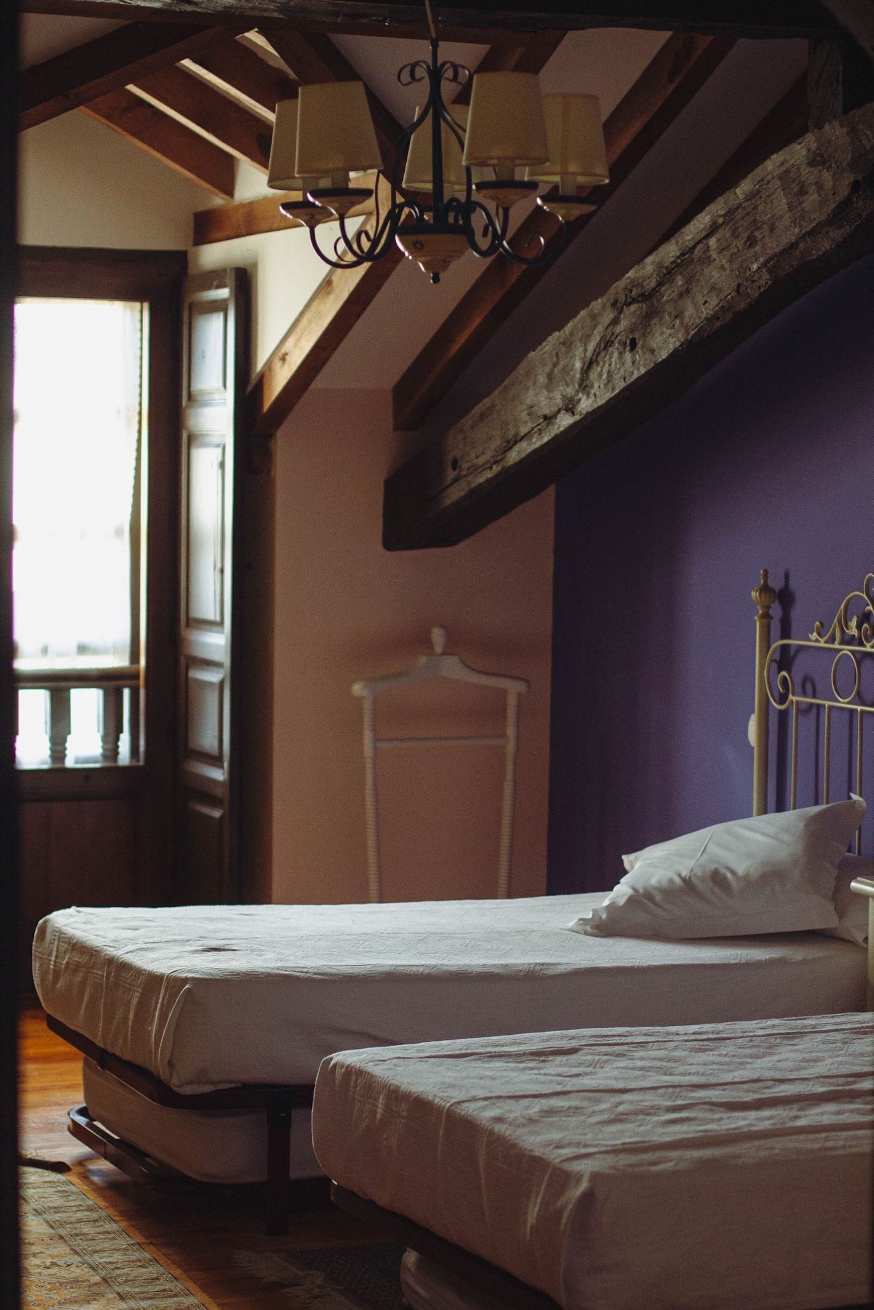 A bedroom with two beds, wooden beams, a hanging lamp, and a window.