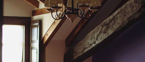 A bedroom with two beds, wooden beams, a hanging lamp, and a window.