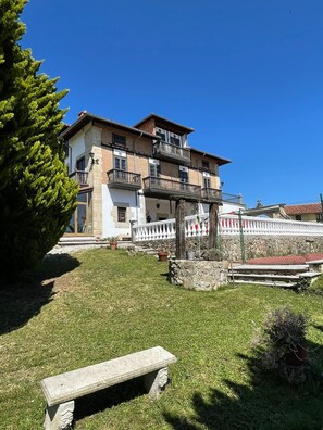 A multi-story building with balconies, a stone wall, and a grassy courtyard with a bench. - Hotel Palacio La Casona de Cerrazo (Reocin)
