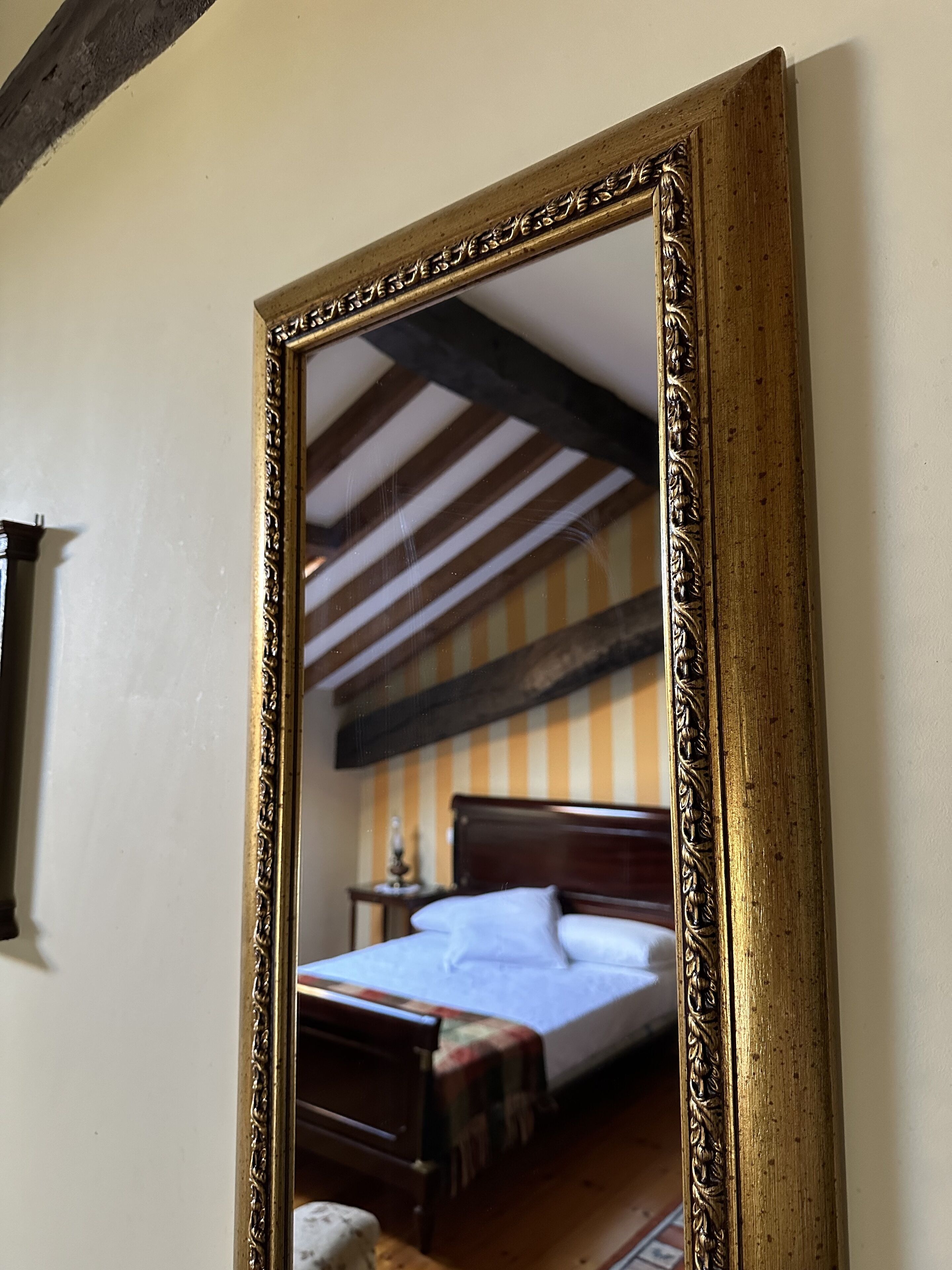 A bedroom with a wooden bed, a nightstand, and a mirror with an ornate frame.