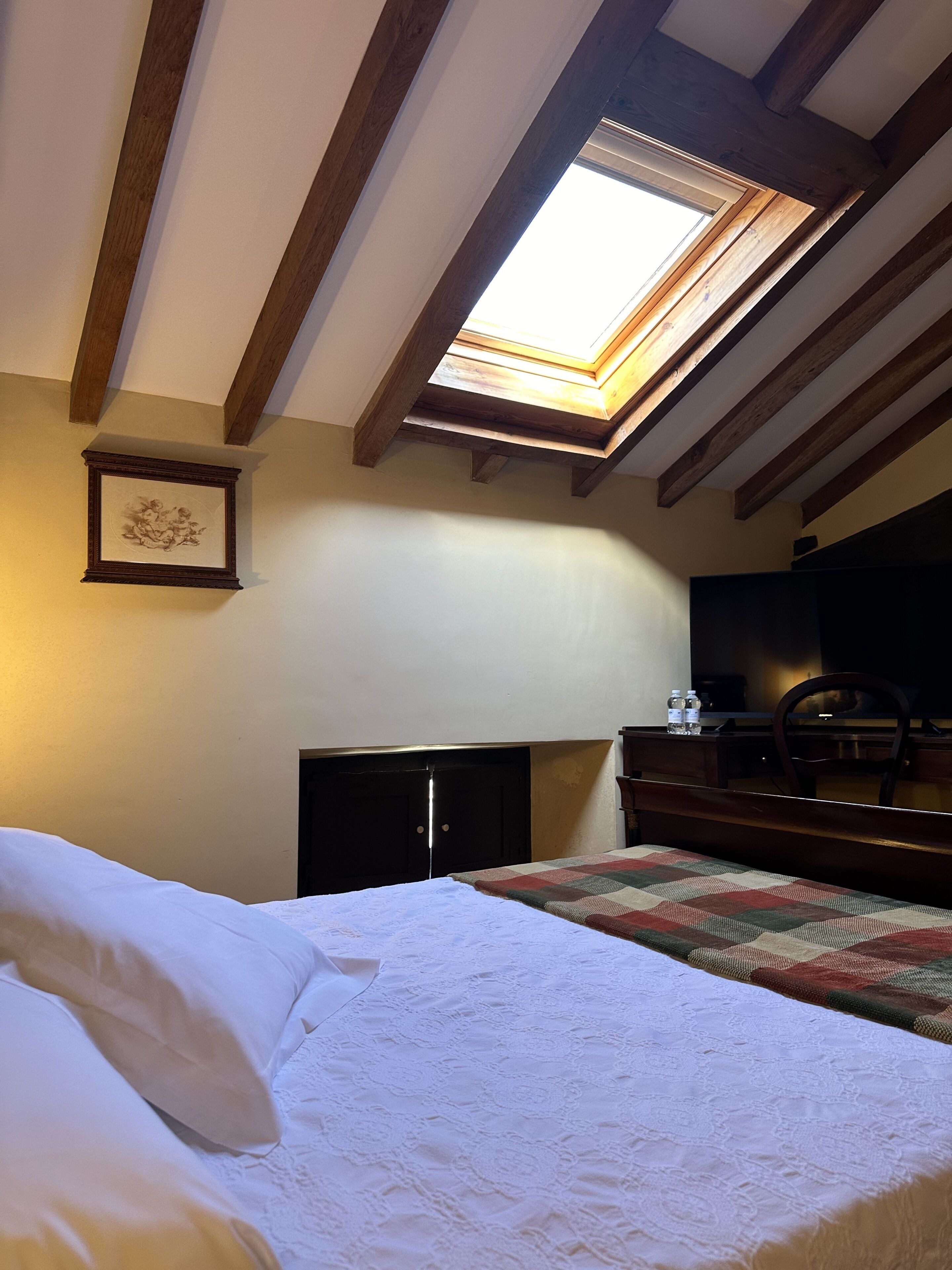 A bedroom with a skylight, a bed with white linens, a wooden dresser, and a desk with a chair.