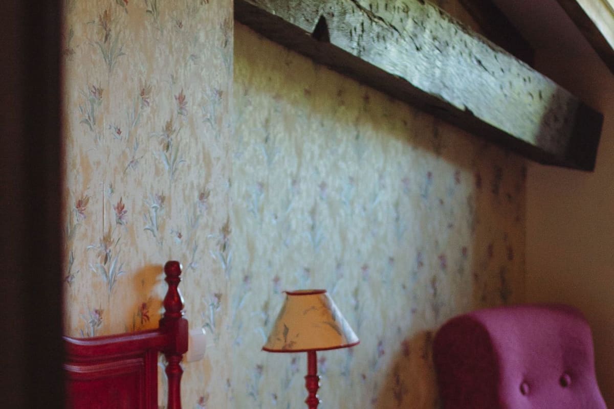 Een slaapkamer met een bed, een rode stoel, een klein tafeltje met een lamp en bloemenbehang.