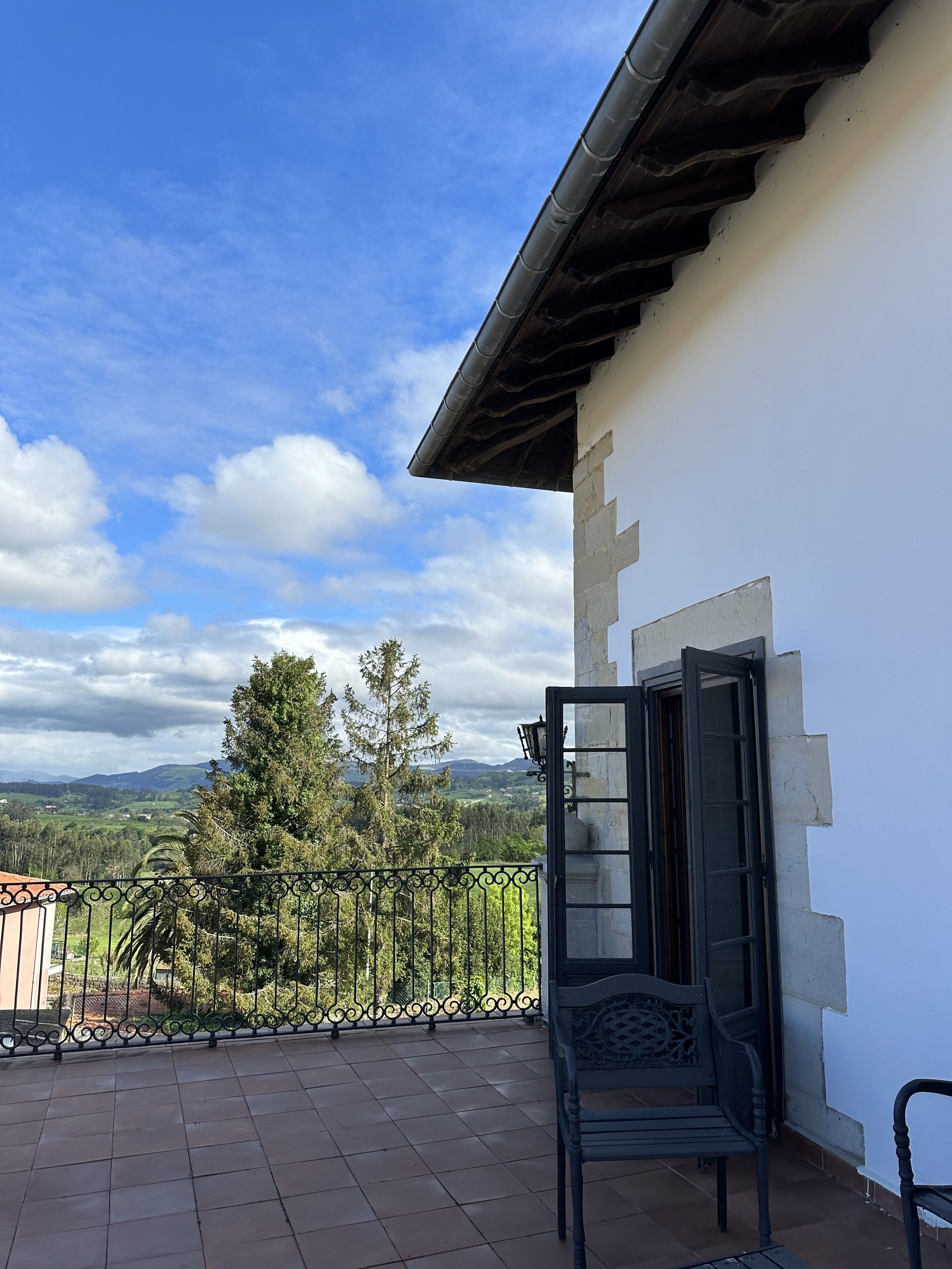 A balcony with a view of a mountainous landscape, a metal railing, and a bench.