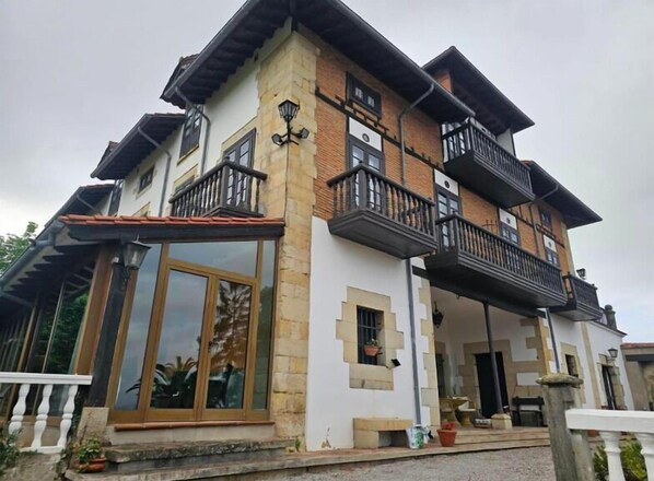 A two-story house with a balcony, large windows, and a stone facade. - Hotel Palacio La Casona de Cerrazo (Reocin)