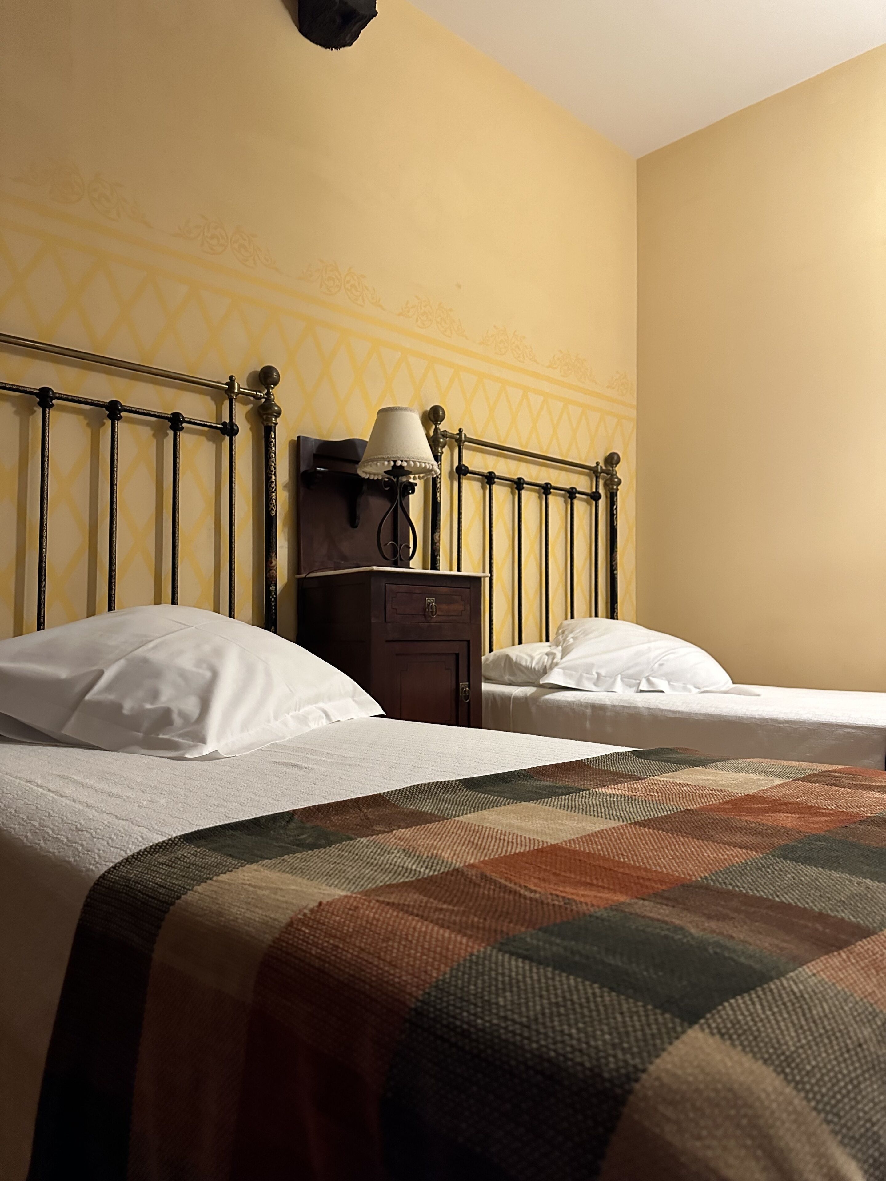 A hotel room with two beds, a nightstand, a lamp, and a patterned wall.