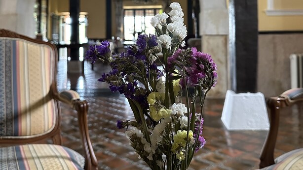 Une pièce dotée d’une grande porte en arc de cercle, d’un lustre et d’un vase rempli de fleurs posé sur un tapis à motifs.