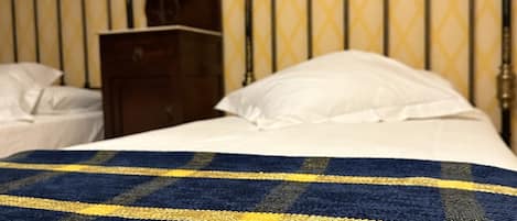 A bed with a blue and yellow checkered blanket, a wooden nightstand with a lamp, and a metal headboard.