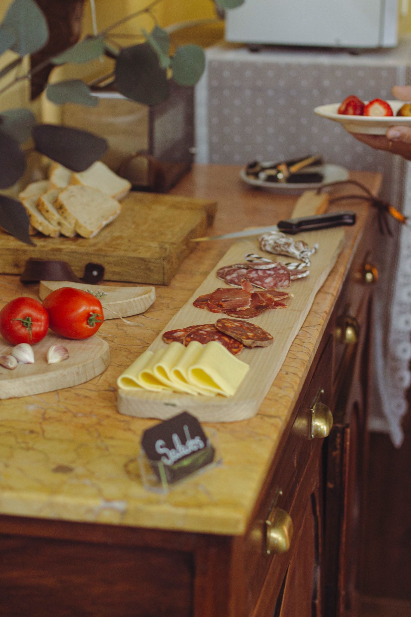 Una encimera de madera con diversos productos alimenticios, entre ellos tomates, ajo, queso y embutidos curados.