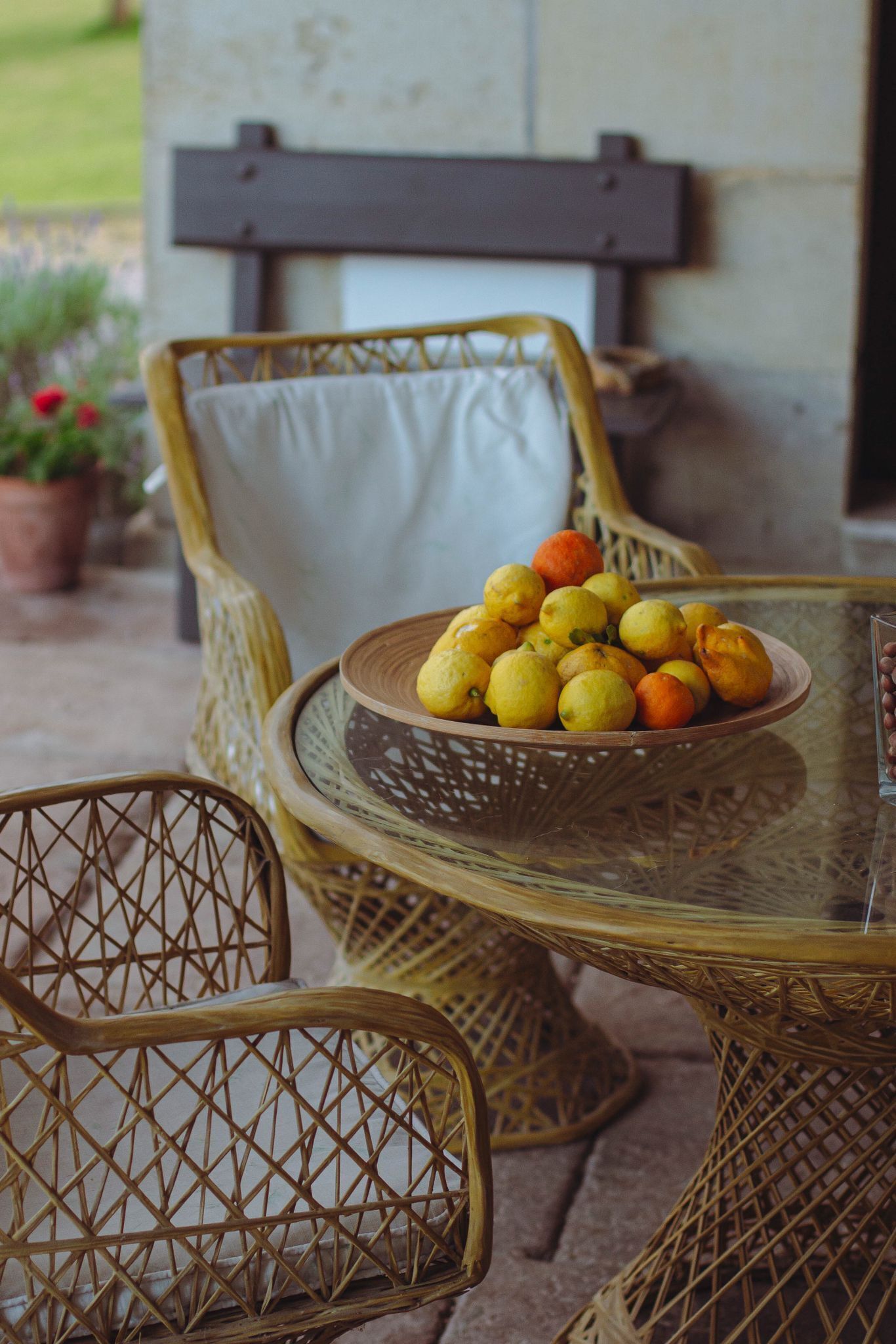 Wicker chairs and a glass table with a bowl of lemons and oranges.