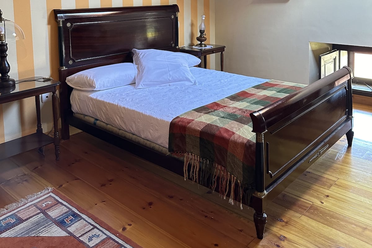 Een slaapkamer met een houten bed, gestreept behang, een dakraam en een houten vloer.