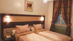 A double bed with a quilted duvet, bedside lamps, a telephone, and a window with curtains. - Hotel St Telemly (Algiers)