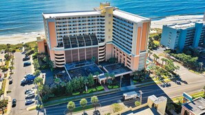 Un hôtel à plusieurs étages doté d’une cour intérieure, entouré d’un parking et offrant une vue sur la plage.