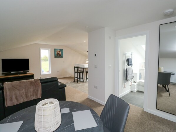 A modern living room with a flat-screen TV, a sofa, a dining table with papers, and a large mirror.