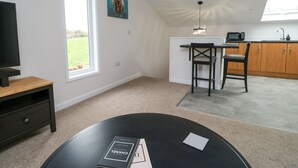 Une cuisine moderne équipée d’un four à micro-ondes, d’un évier et de meubles en bois. On y trouve un coin repas avec deux chaises et une table. Un téléviseur est fixé au mur, et un tableau représentant un taureau est visible.