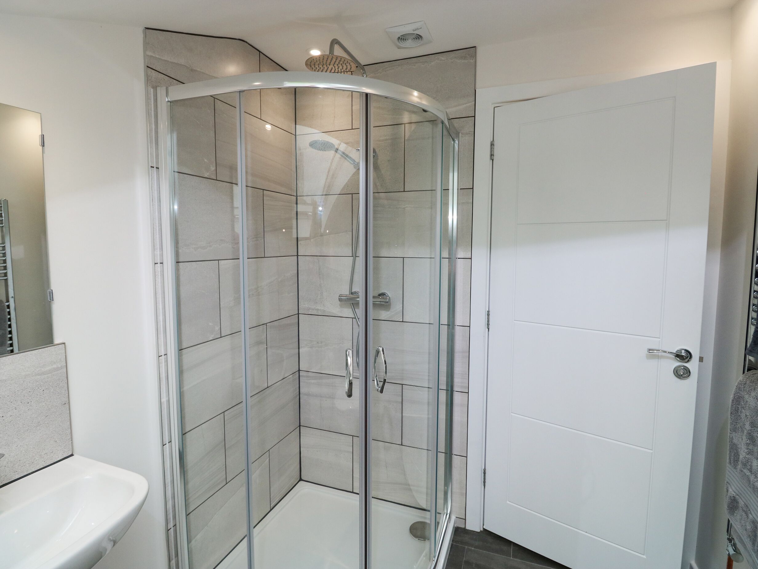 Une salle de bain moderne avec une douche à parois de verre, un lavabo blanc et une porte.