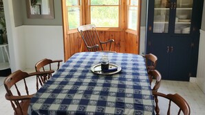 Un coin repas avec une nappe à carreaux, des chaises en bois, une fenêtre donnant sur la verdure et un buffet aux portes vitrées.