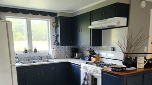 Une cuisine avec des meubles de couleur bleu foncé, un four blanc et une fenêtre donnant sur un paysage verdoyant.