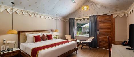 A hotel room with a large bed, a desk, a chair, a ceiling fan, and a window with curtains.