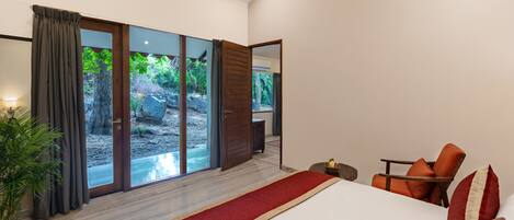 A modern bedroom with a large bed, a wooden chair, a small table, and a view of a garden through sliding glass doors.