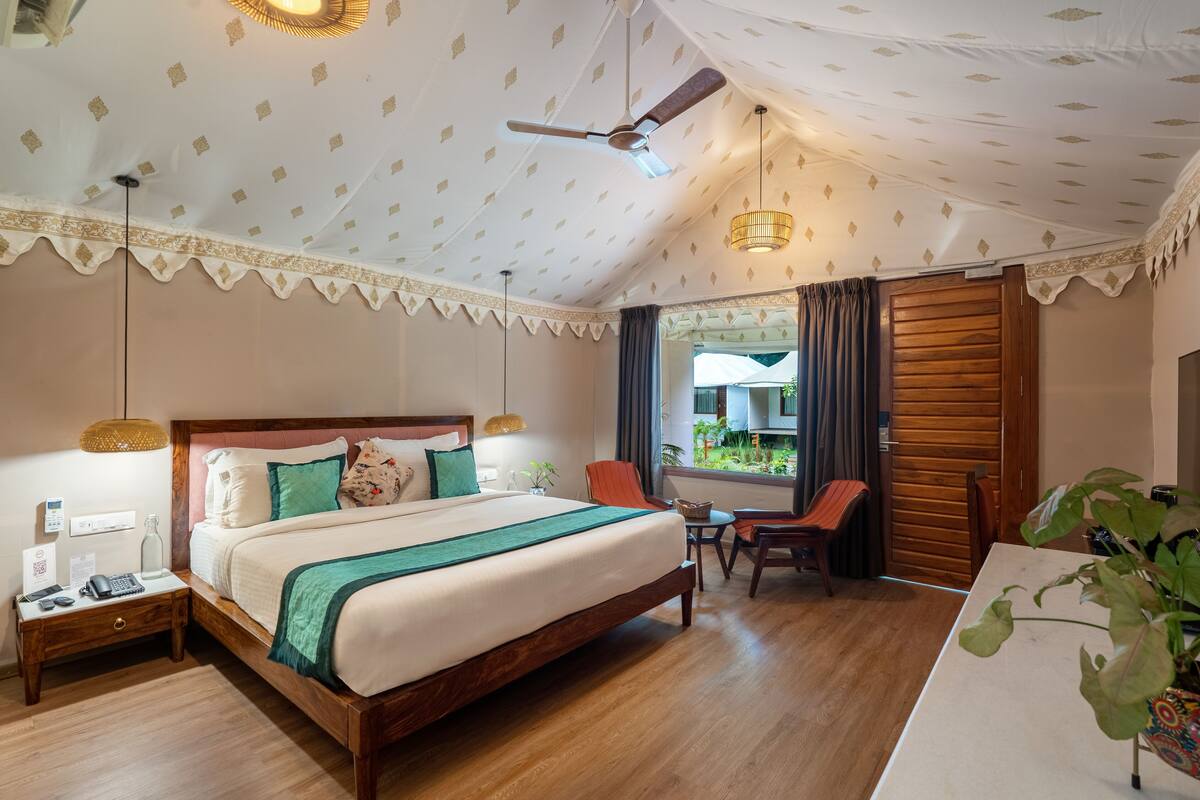 A hotel room with a large bed, a desk, a chair, a ceiling fan, and a window with curtains.