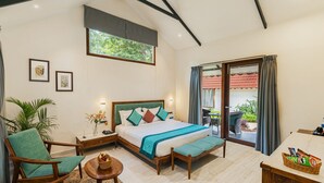 Ein geräumiges Schlafzimmer mit einem großen Bett, einer Sitzecke mit Sessel und kleinem Tisch, einem Nachttisch und Blick ins Freie durch eine Schiebetür.