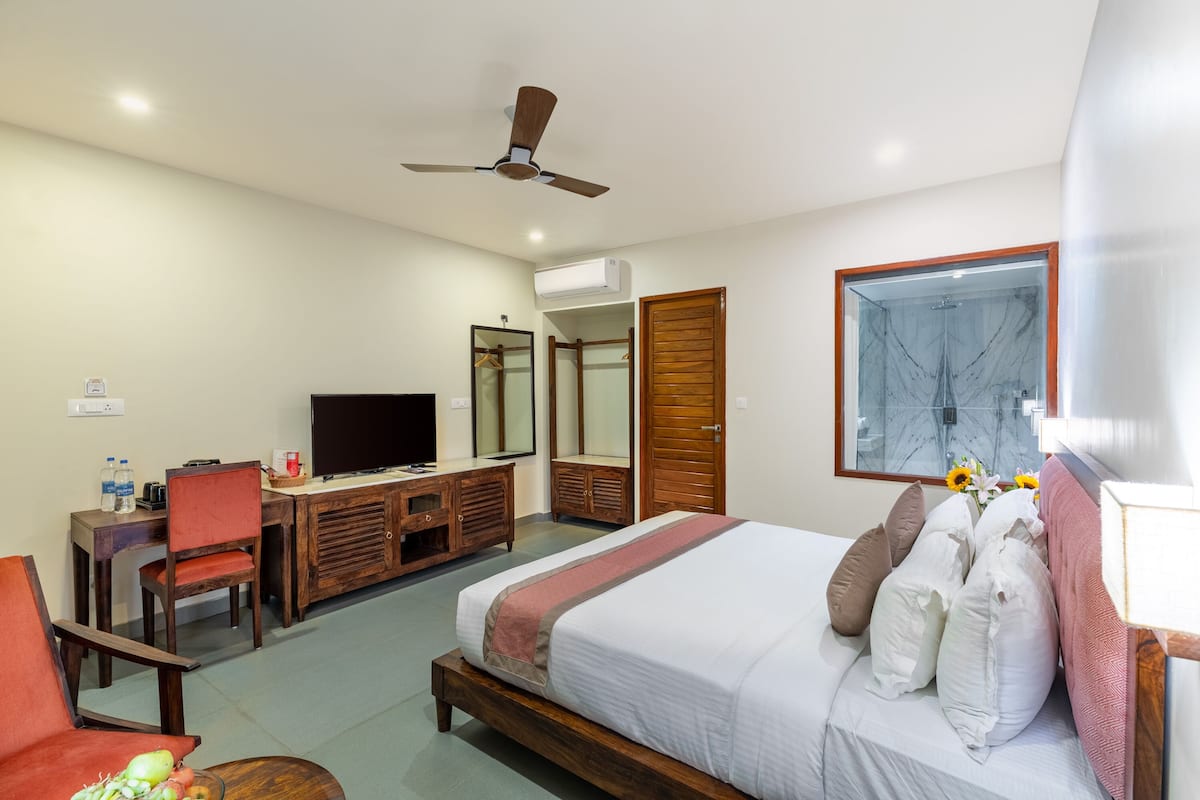 A hotel room with a bed, a desk, a television, a wardrobe, and a ceiling fan.