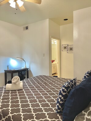 Ein Hotelzimmer mit Bett, Schreibtisch mit Lampe, Deckenventilator und Tür zu einem Badezimmer.