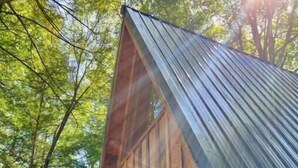 Uma cabana de madeira com telhado inclinado, porta frontal e pequena varanda.