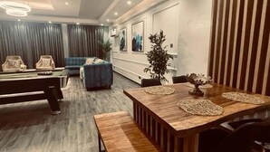 A modern living room with a pool table, a blue sofa, and a dining table with placemats. - RBT Hotel (Lagos)