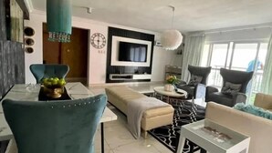 A modern living room with a sofa, a TV mounted on the wall, and a dining area with a table and chairs. - RBT Hotel (Lagos)