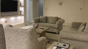 A modern living room with a sectional sofa, a coffee table, and a flat-screen TV mounted on the wall. - The Palms Hotel (Abuja)