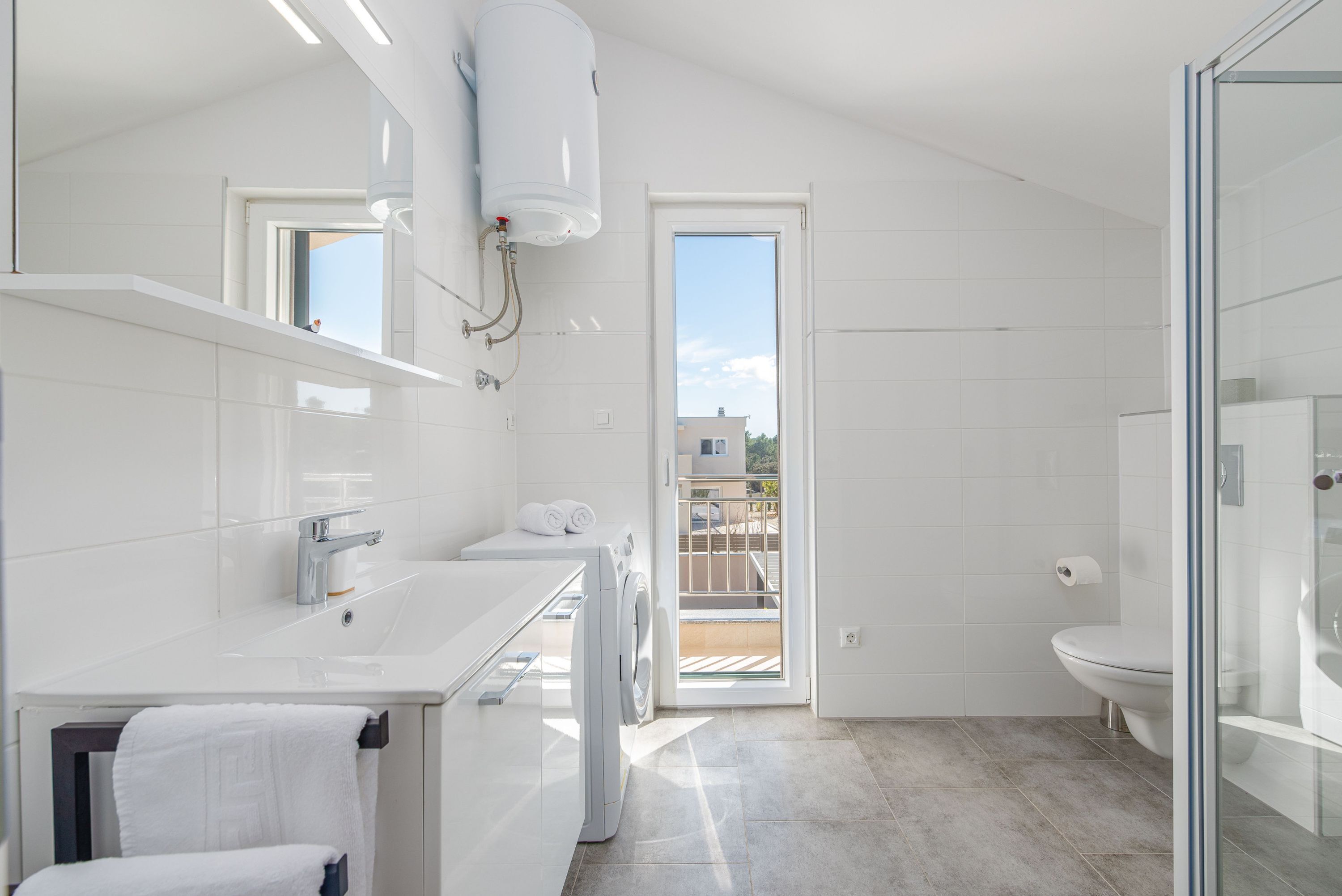A modern bathroom with a built-in washing machine, a large mirror, and a glass shower enclosure.