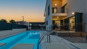A swimming pool with lounge chairs, a covered seating area, and a building with balconies and a staircase. - Villa Kristina Zadarvillas (Nin)