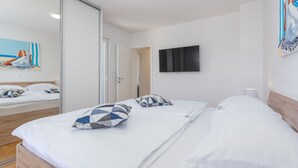 A hotel room with a bed, a TV mounted on the wall, and a painting on the wall. - Villa Kristina Zadarvillas (Nin)