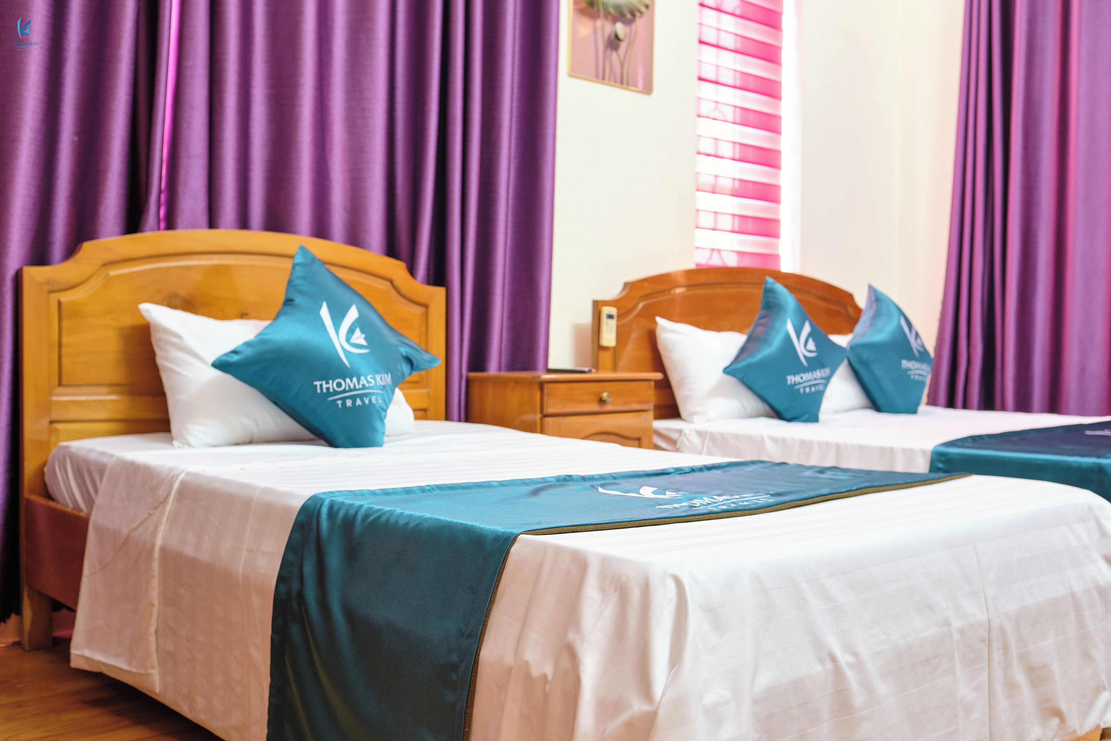 Two beds with matching headboards and pillows, a wooden nightstand, and purple curtains.