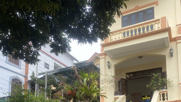 An outdoor seating area with chairs and tables, surrounded by potted plants and a building with a balcony. - Kim Homestay & Villa (Bai Chay)