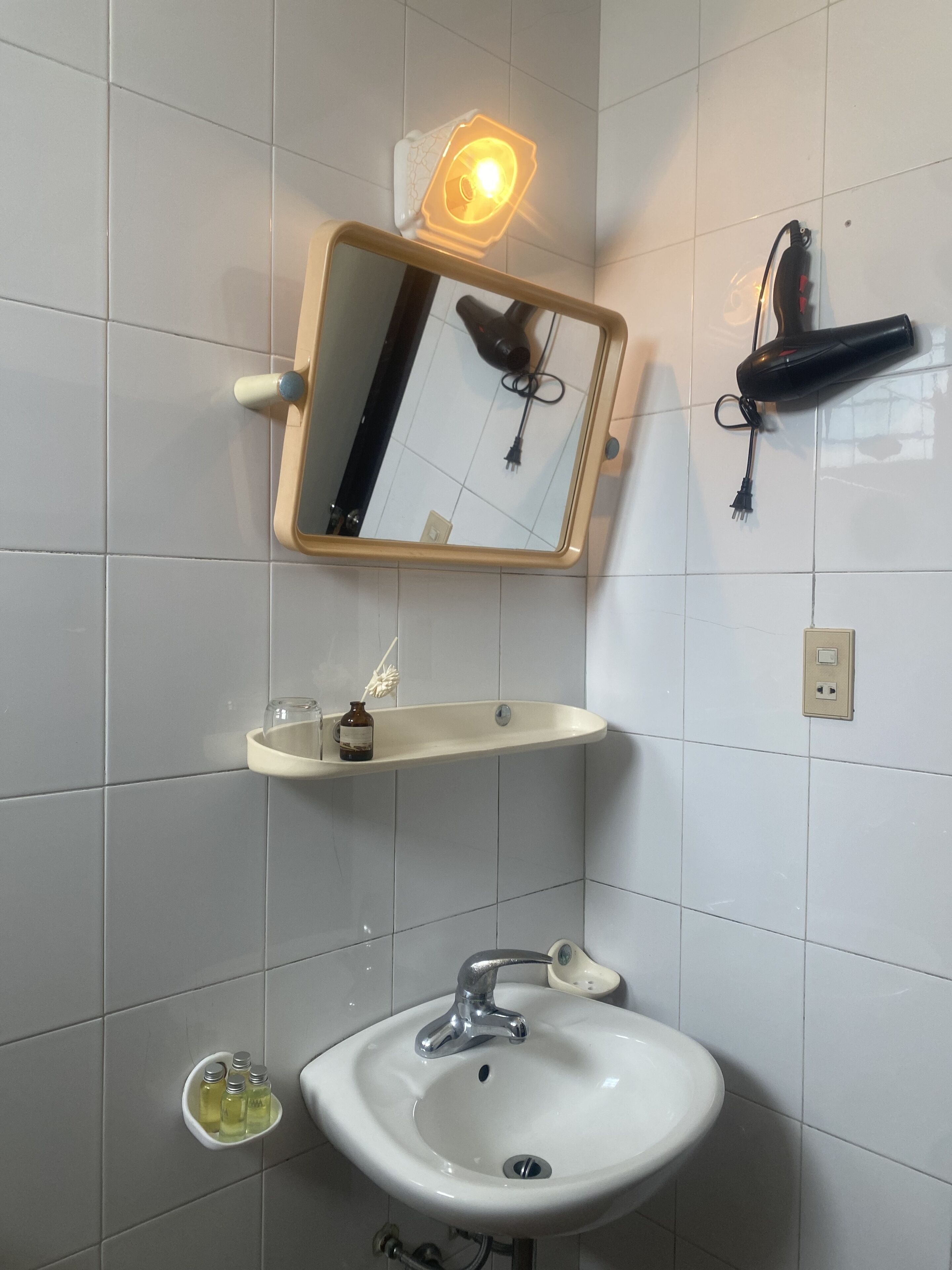 A bathroom with a white sink, a mirror, and a hairdryer mounted on the wall.