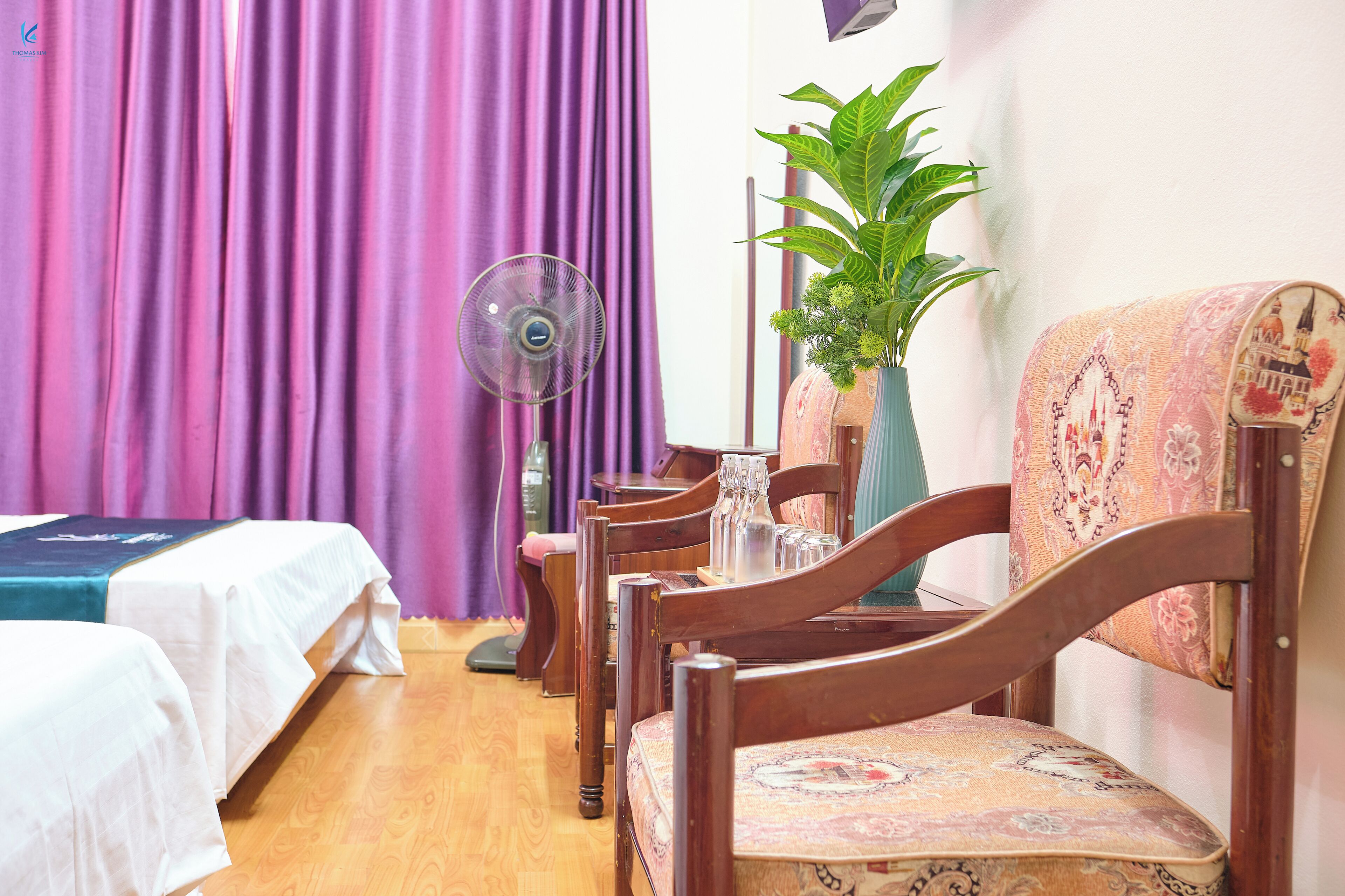 A hotel room with two beds, a wooden chair, a table with a vase, and a potted plant.