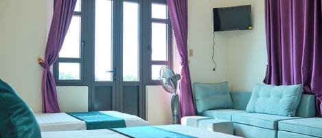 A hotel room with two beds, a sofa, a TV, and a window with purple curtains.