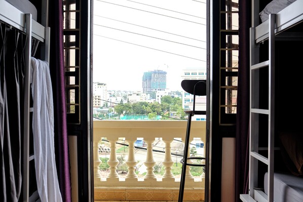 Una habitación con vista a un paisaje urbano a través de una ventana abierta, una baranda de balcón y una farola.