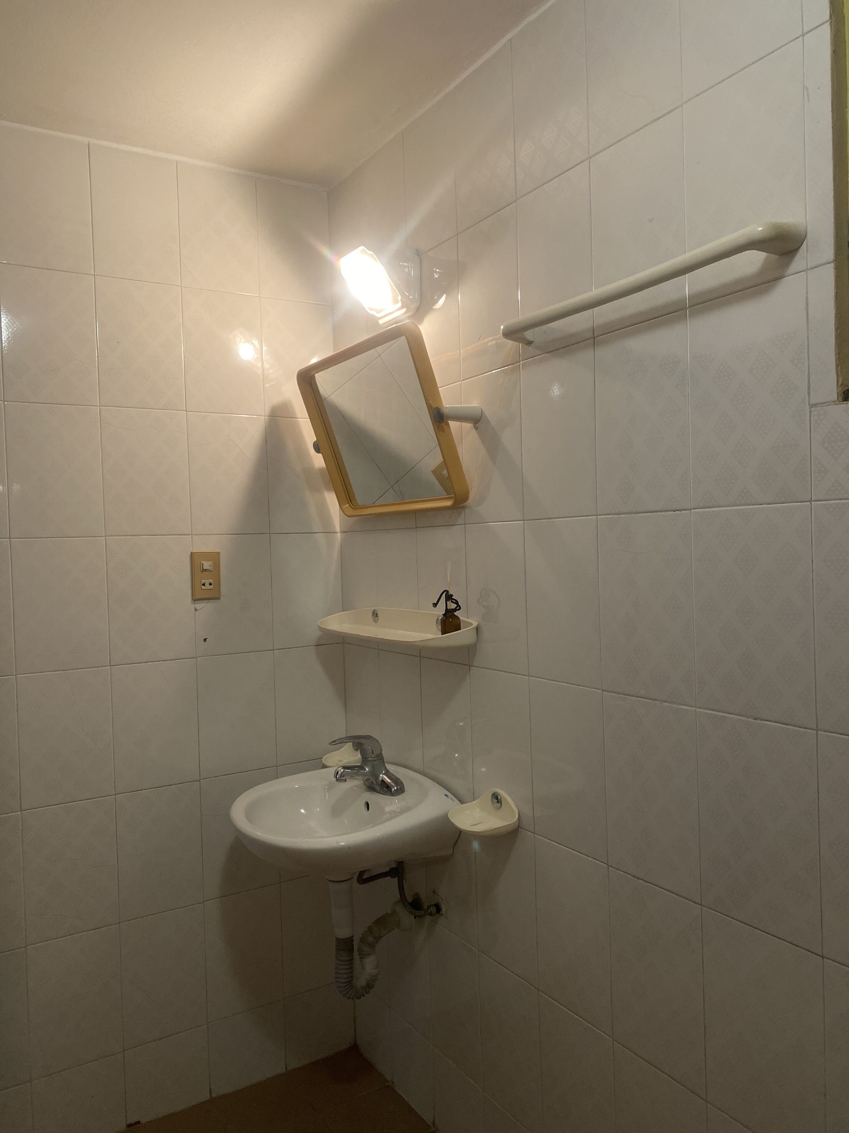 Un baño con paredes de azulejos blancos, un lavamanos con espejo y un perchero para toallas.