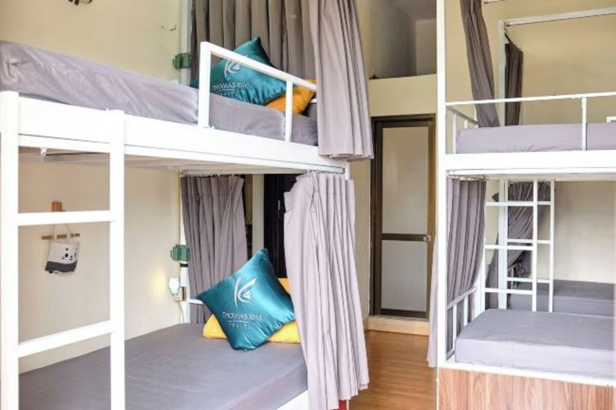 A room with bunk beds, curtains, a small table, and a bag hanging on the wall.